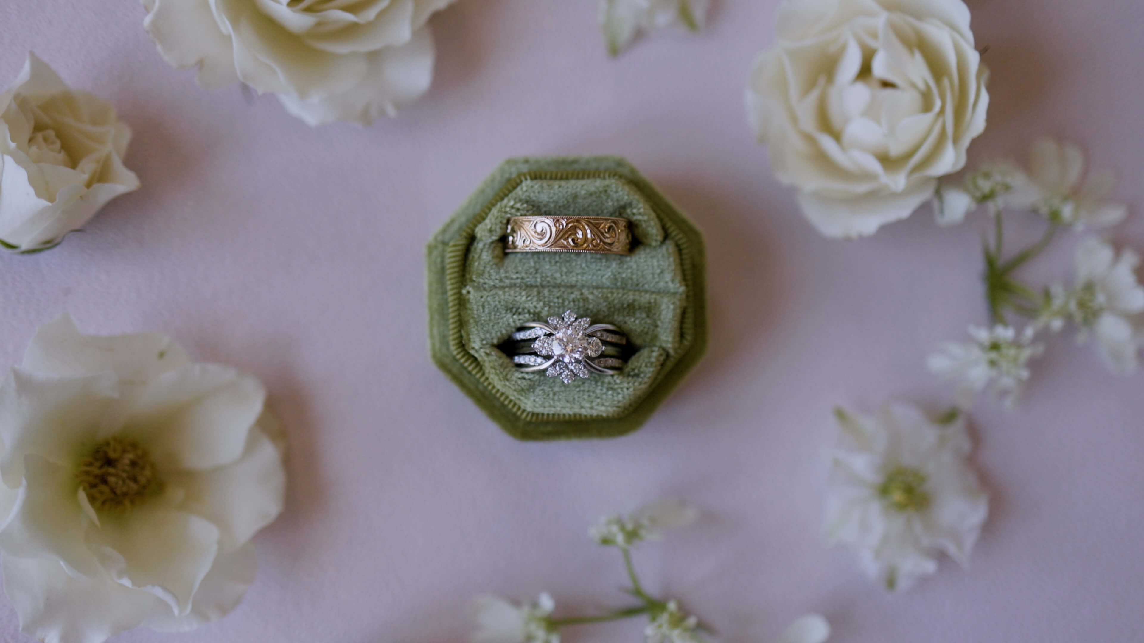 Intricate wedding rings in a green box surrounded by white flowers