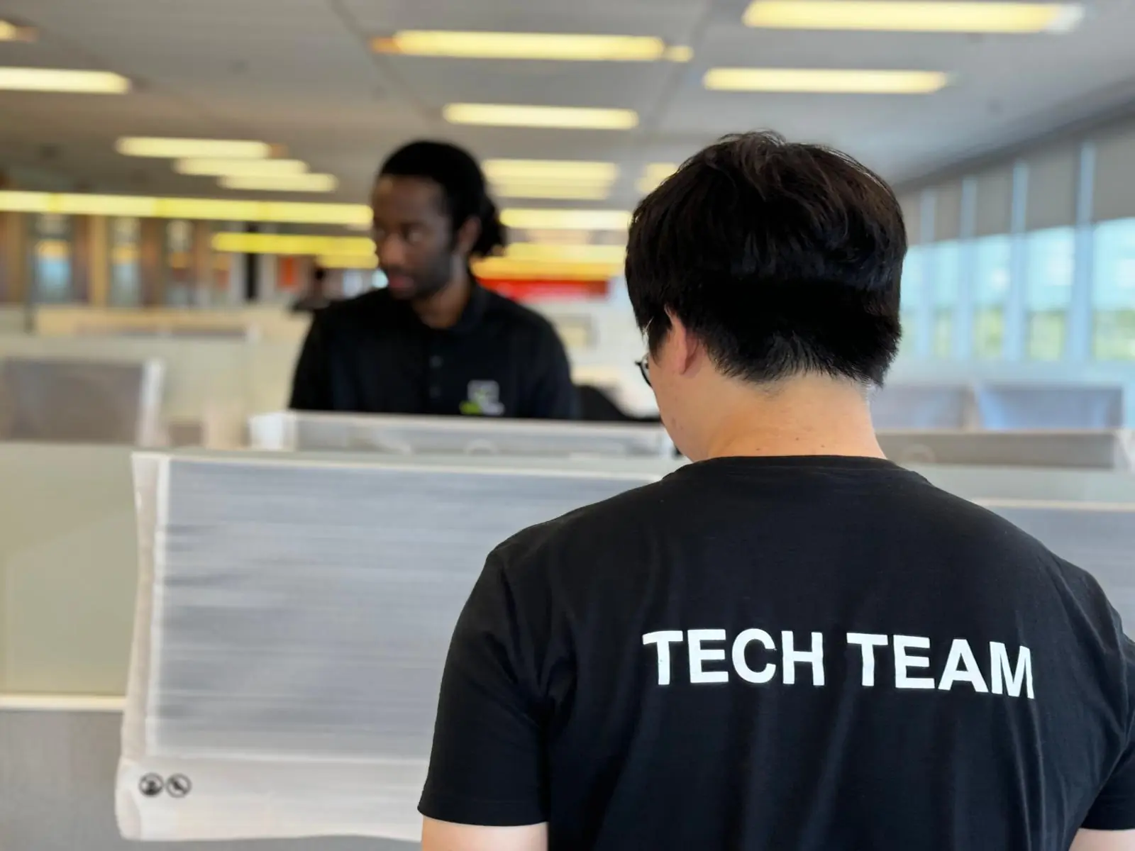 IT support technician wearing “Tech Team” shirt assisting with workstation setup in a professional office environment