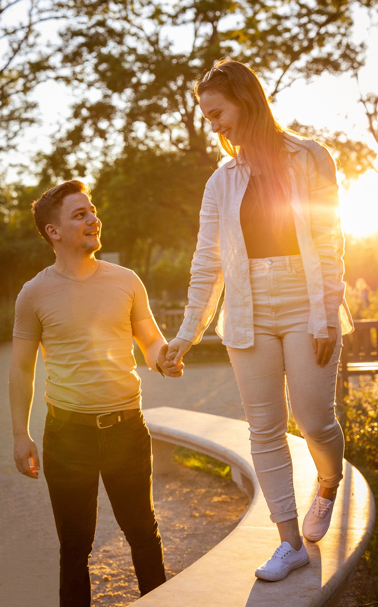 Egy pár kézen fogva sétál naplementében, a nő egy emelvényen áll.