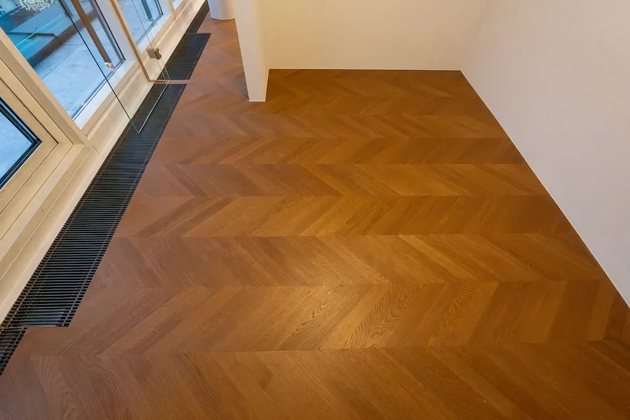 Heller Raum mit stilvollem Chevron-Parkettboden und bodentiefem Fensterbereich.