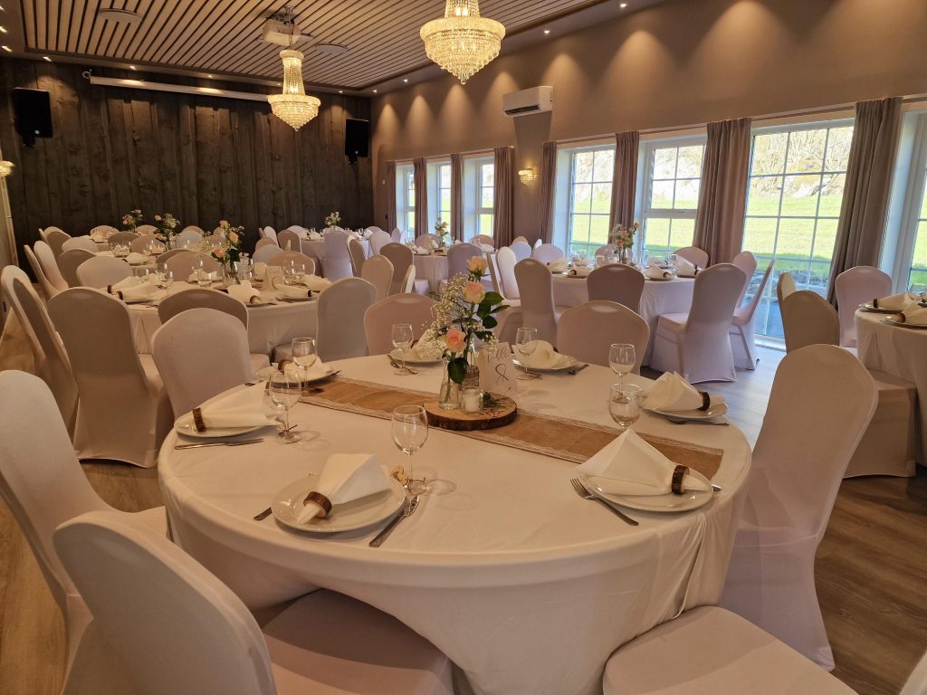 An elegant wedding ceremony setup features a domed gazebo adorned with peach and pink floral arrangements and lush greenery. White chairs line the aisle.