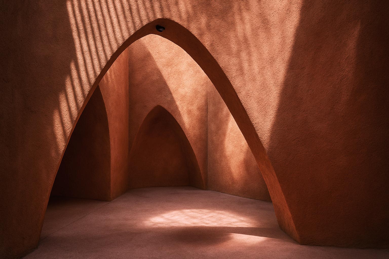 Terracotta stucco space with intersecting arches and warm sunlight creating geometric shadows.