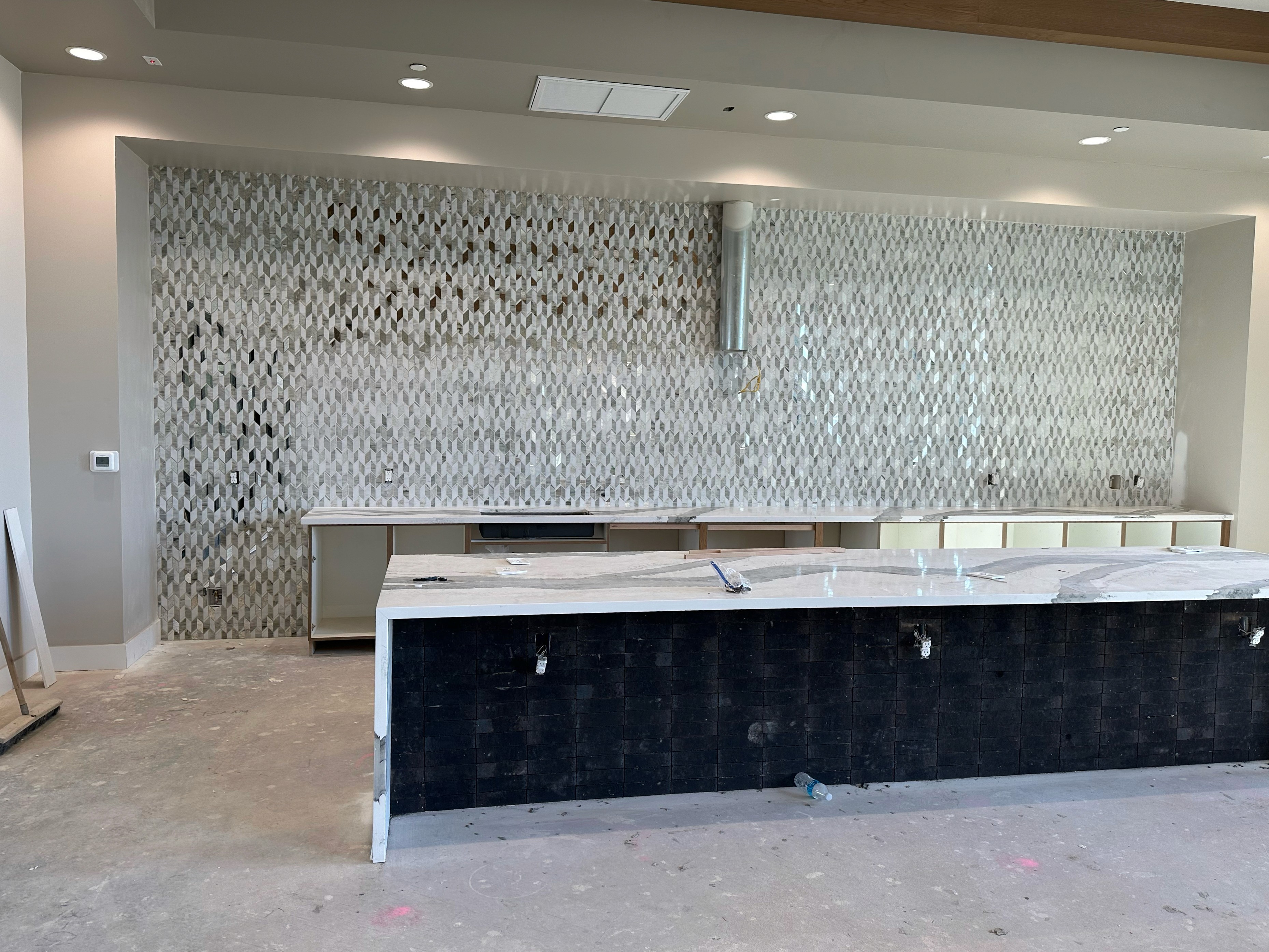 Contemporary kitchen with a white marble countertop and intricate patterned tile backsplash under a range hood.