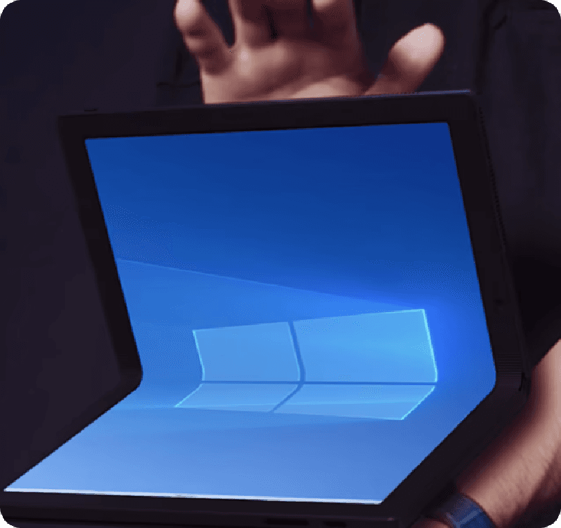 Hands hold open a futuristic, foldable laptop displaying the Windows 11 logo on its vibrant blue screen.