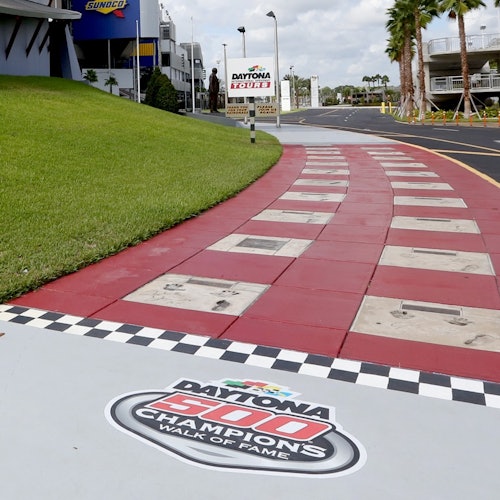 En rød og hvid ternet gangsti med håndaftryk og underskrifter, mærket "Daytona 500 Champions Walk of Fame," på et motorsportssted.
