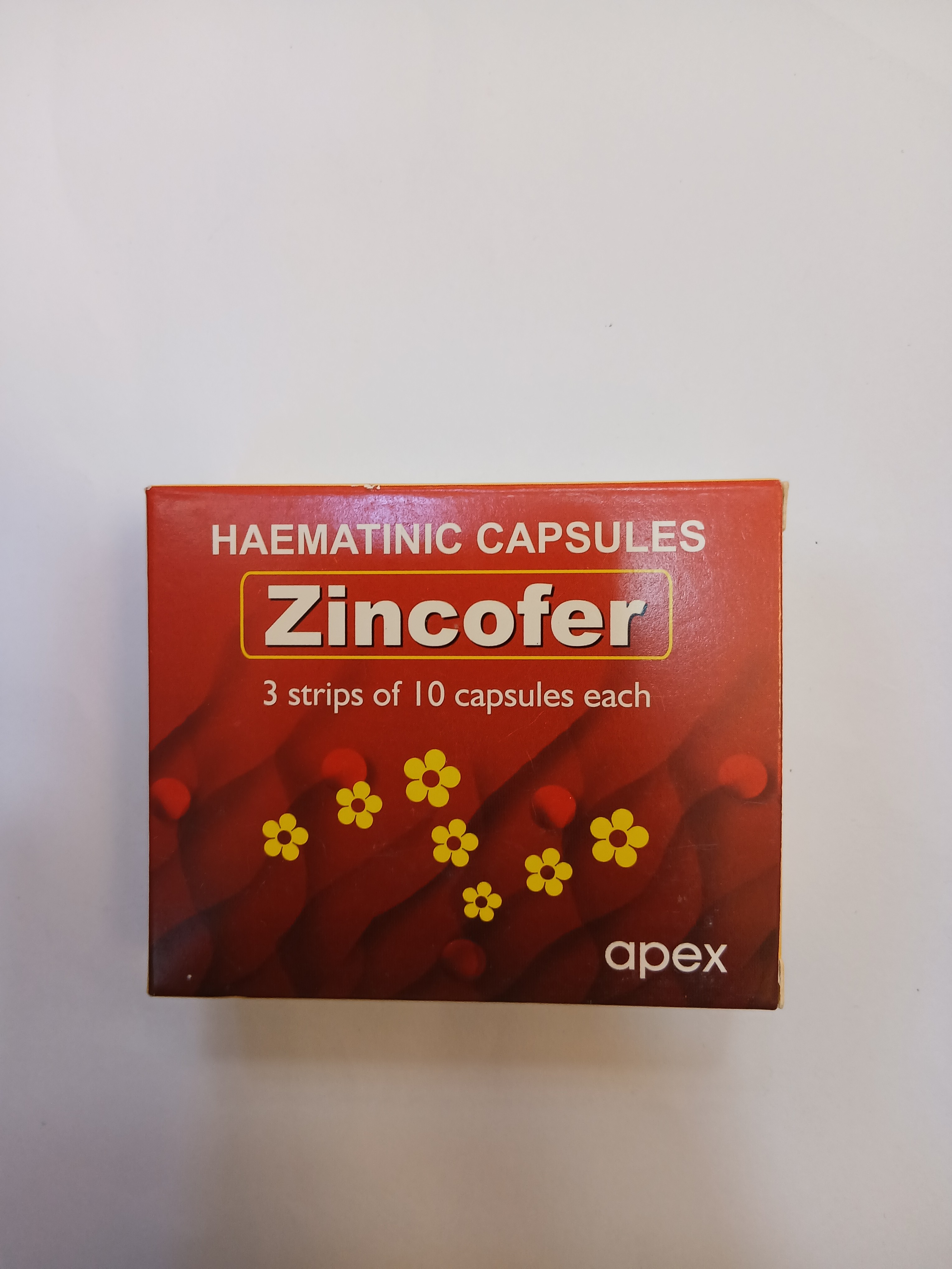 A red cardboard box with white and yellow text displays three blister strips of ten capsules each, featuring yellow flower illustrations on the front.