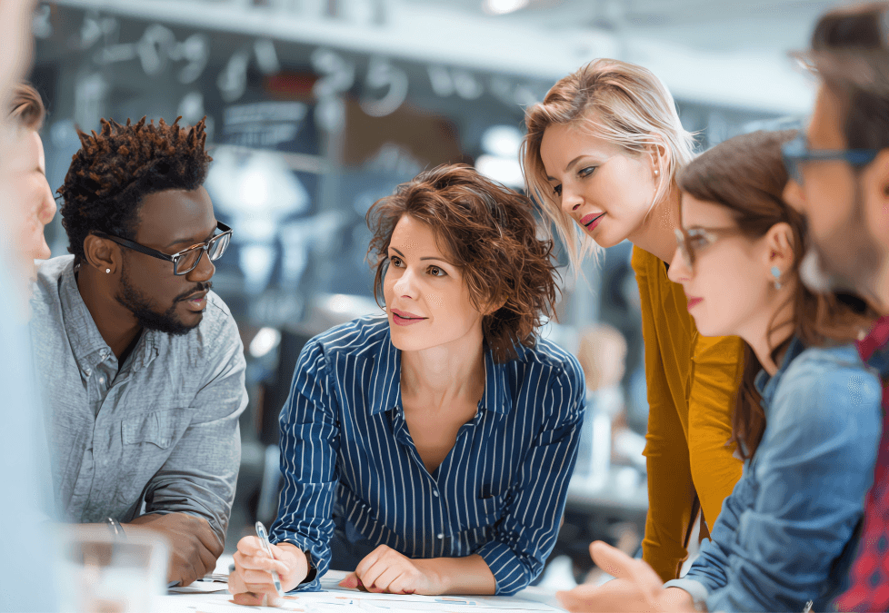 A diverse group of professionals collaborates around a table in a modern office, with a focus on a woman in a striped shirt discussing a project, embodying teamwork and communication.
