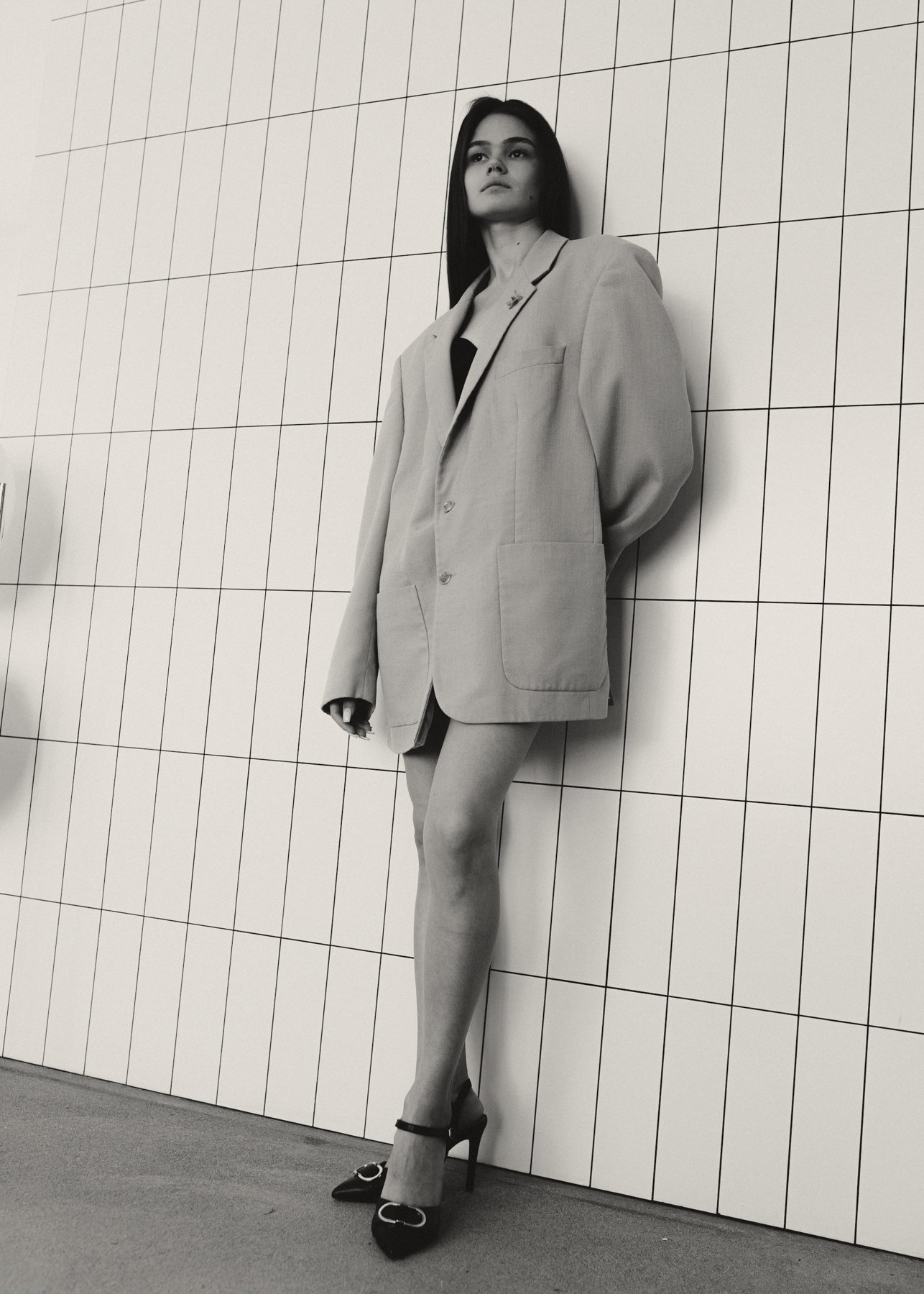 Model against a tiled wall in an oversized putty blazer
