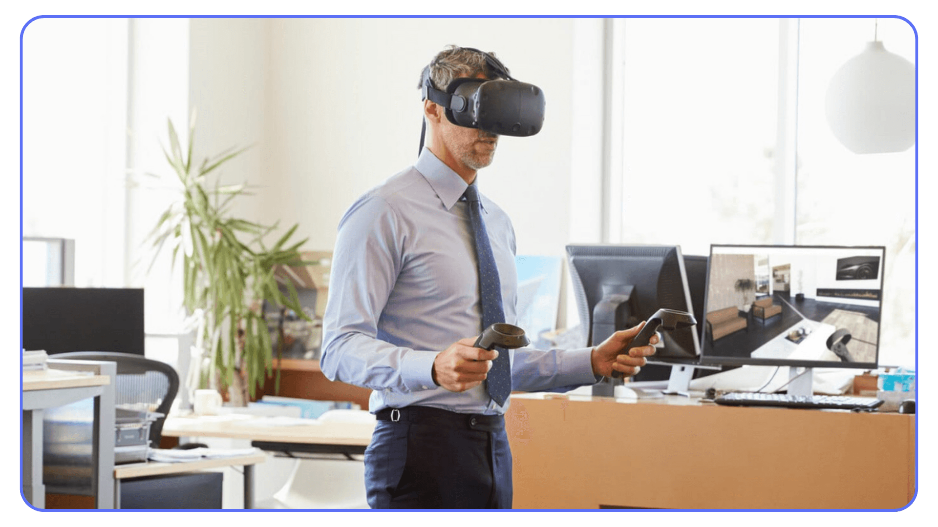 Business professional wearing a VR headset and holding controllers in a modern office, with a computer behind him displaying a virtual interior scene.