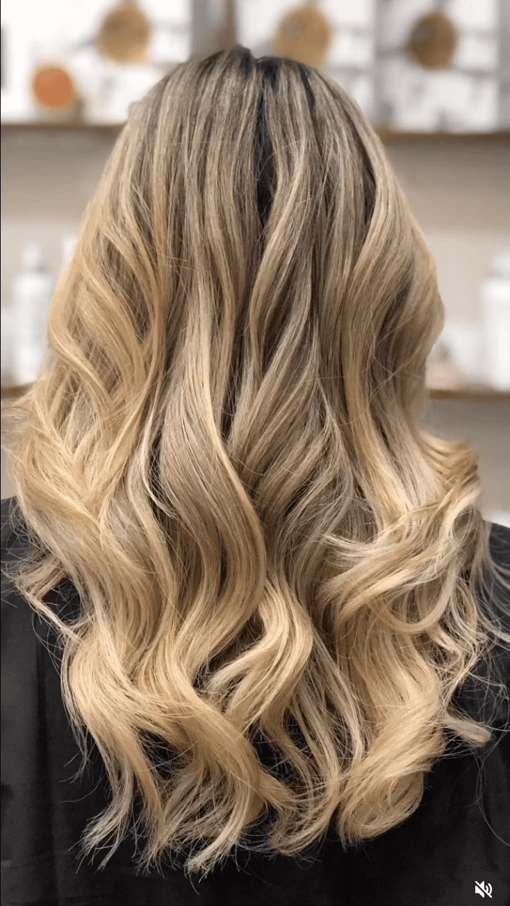 Back view of long, blonde hair with dark root melt and dimensional balayage, styled in soft beachy waves.