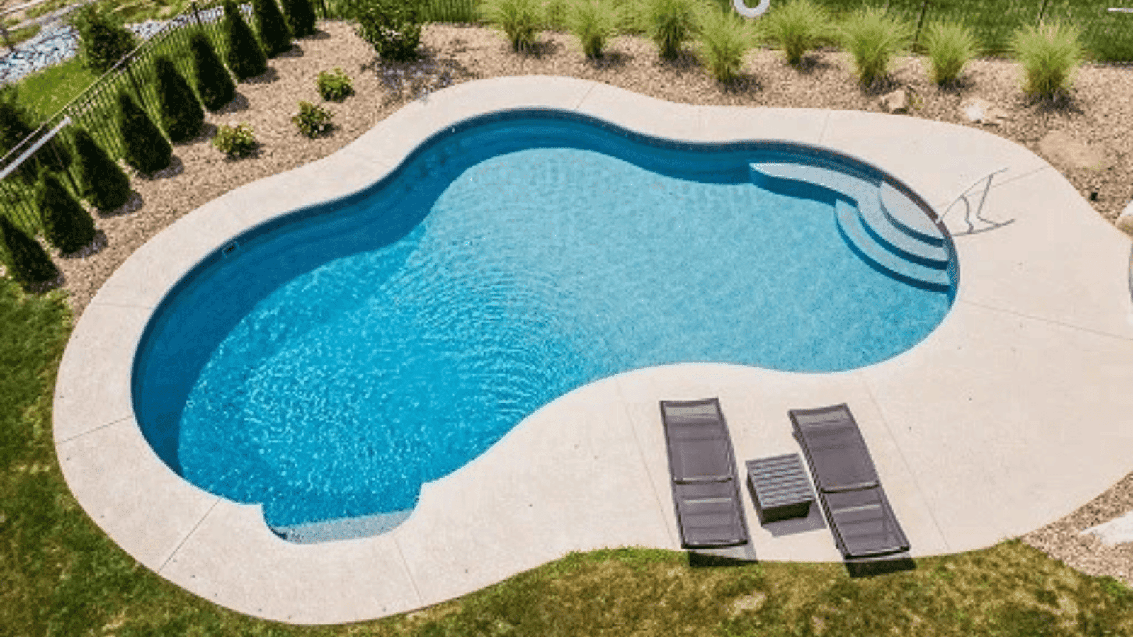 Stunning freeform fiberglass swimming pool installation with concrete deck and built-in steps, showcasing a residential backyard oasis made by Premier Pool Co