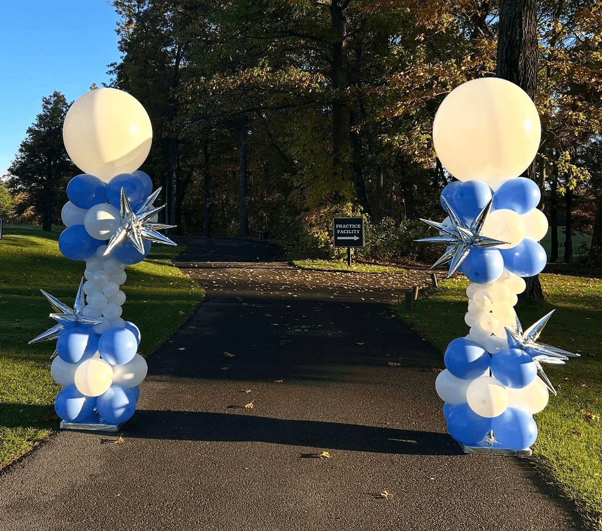 Blue and white balloon columns with large white balloons on top framing a park walkway designed by Be Bold Balloons