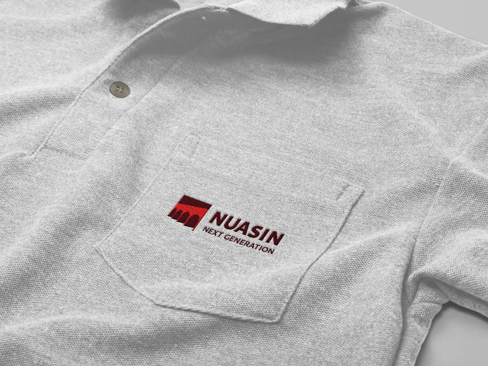 The Nuasin logo embroidered on the chest pocket of a gray polo shirt. 