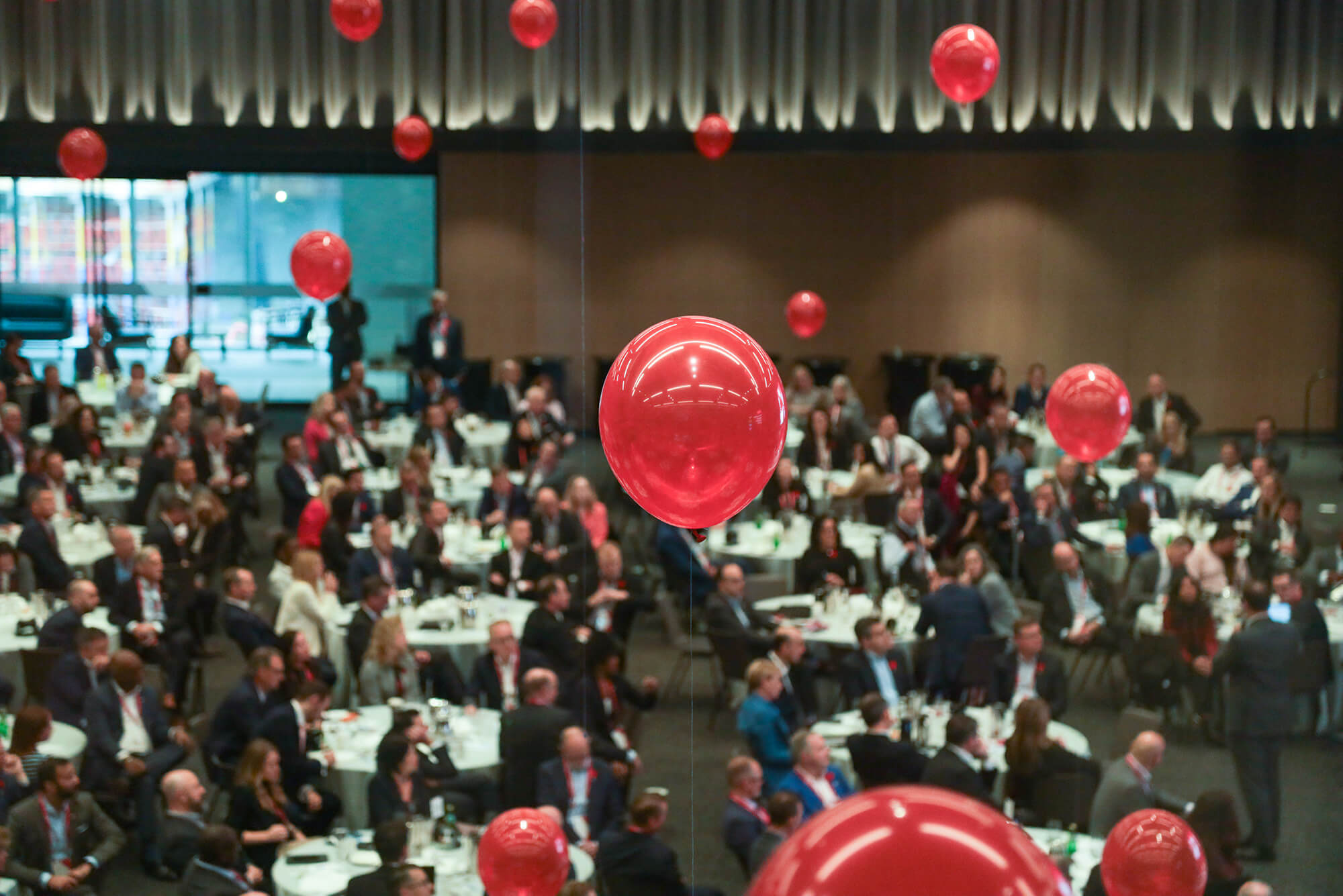 Bright red balloons floating at different heights in a full conference hall.