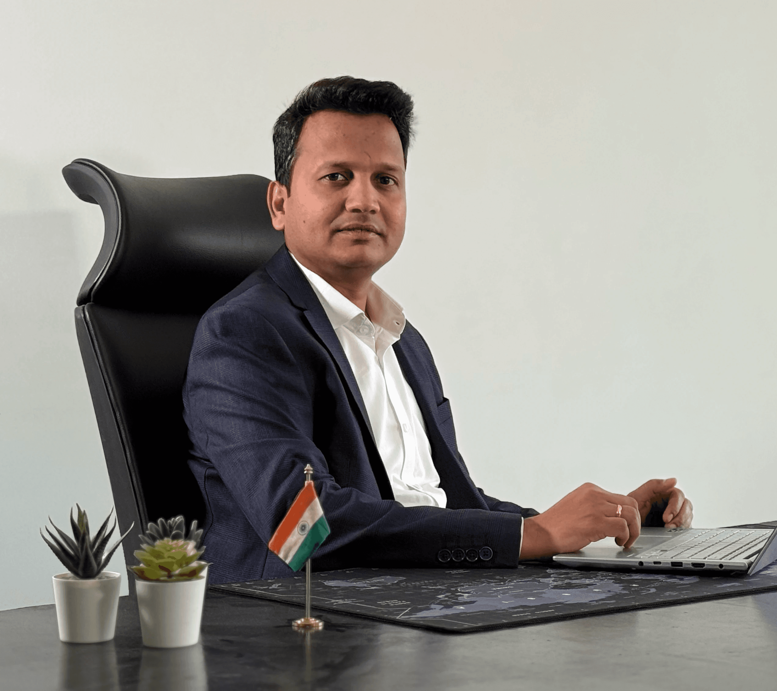 Young adult wearing a navy coat and white turtleneck, looking directly with a neutral expression. The background is plain and light-colored.
