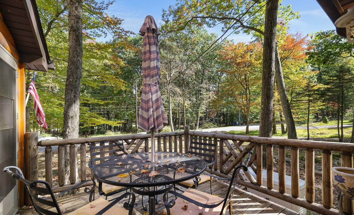Wood deck with patio table and umbrella overlooking the trees at Barefoot Bungalow, Lake Harmony, PA