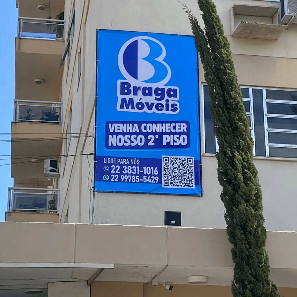 Anúncio da loja Braga Móveis em Bom Jesus do Itabapoana, com destaque para a fachada e placa promocional convidando clientes a conhecer o segundo piso da loja. Inclui contatos telefônicos e QR code para mais informações.