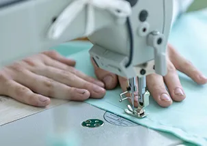A person is sewing a piece of fabric with hand and using a sewing machine. The hand the sewing machine bed and the fabric is visible on the image 