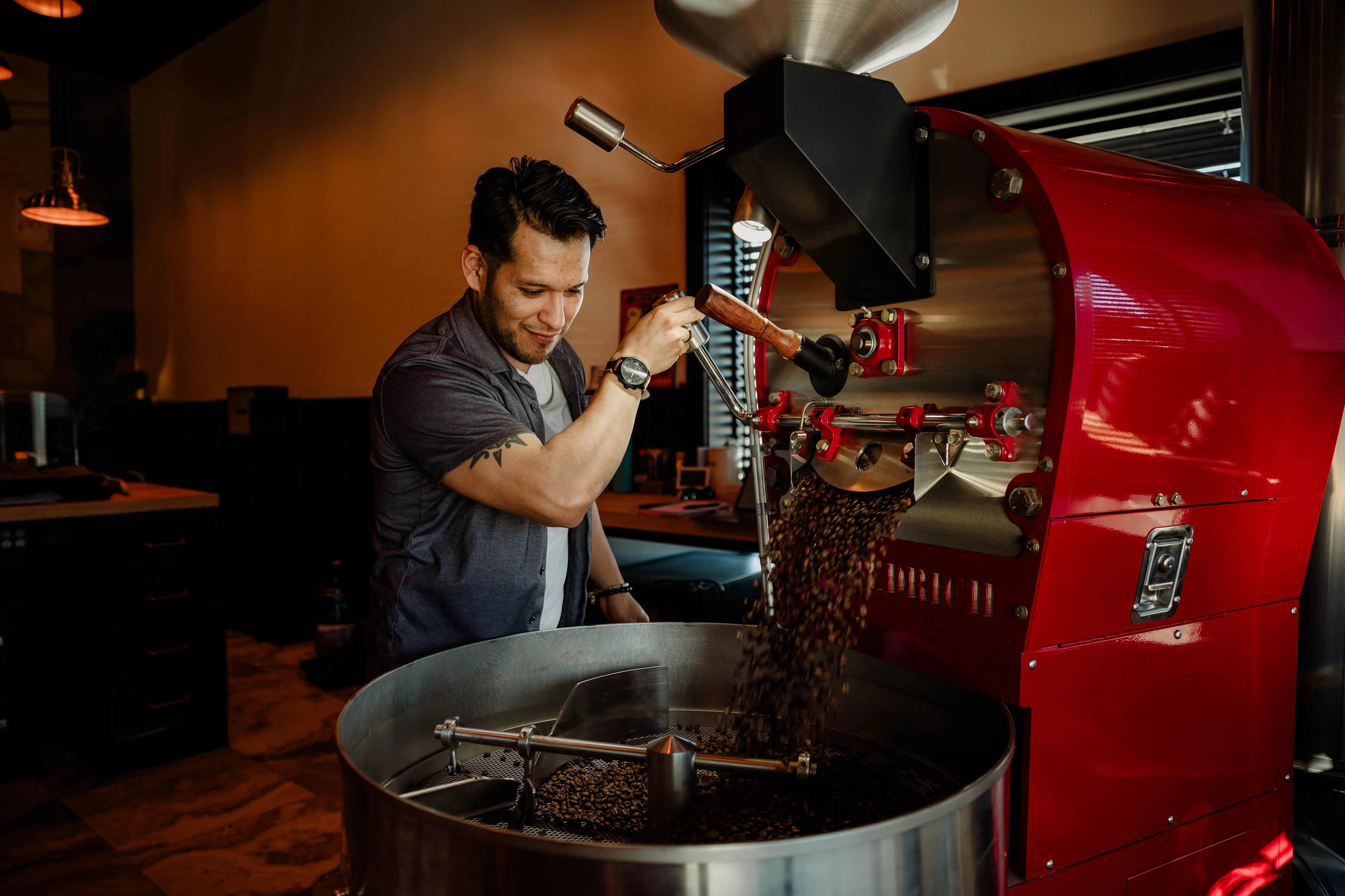 Pain d'Avignon roaster operating the red coffee roasting machine — freshly roasted beans cascading into the cooling tray