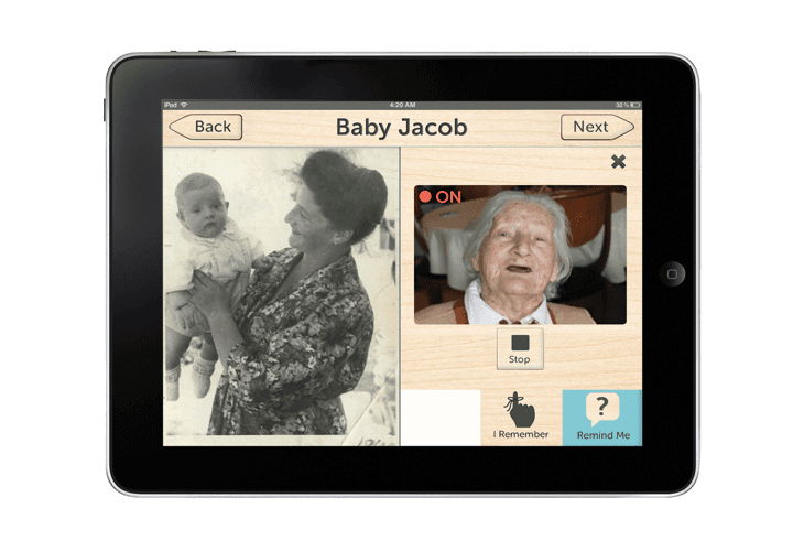 An iPad displays a photo interface showing a black and white photo of a woman holding a baby on the left and a larger, older woman on the right. The text “Baby Jacob” is at the top center, and “Next” appears in the top right corner. Below the photo are buttons labeled “Back” and “Next,” and a “Stop” button is visible near the bottom right. Below the photo are buttons labeled “I Remember” and “Remind Me,” with a question mark icon next to “Remind Me.” The time displayed at the top is 4:20 AM.
