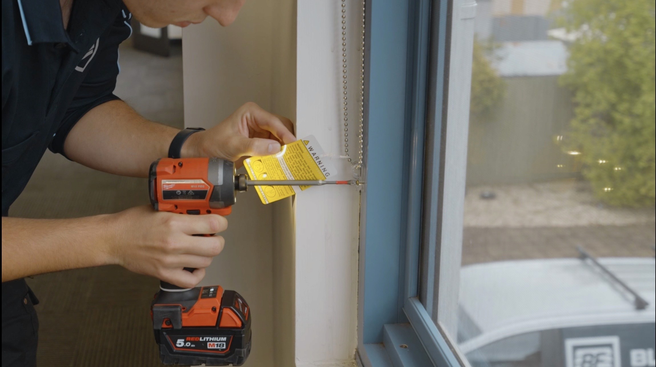Technician securing chain tensioner for roller blind with Milwaukee power drill