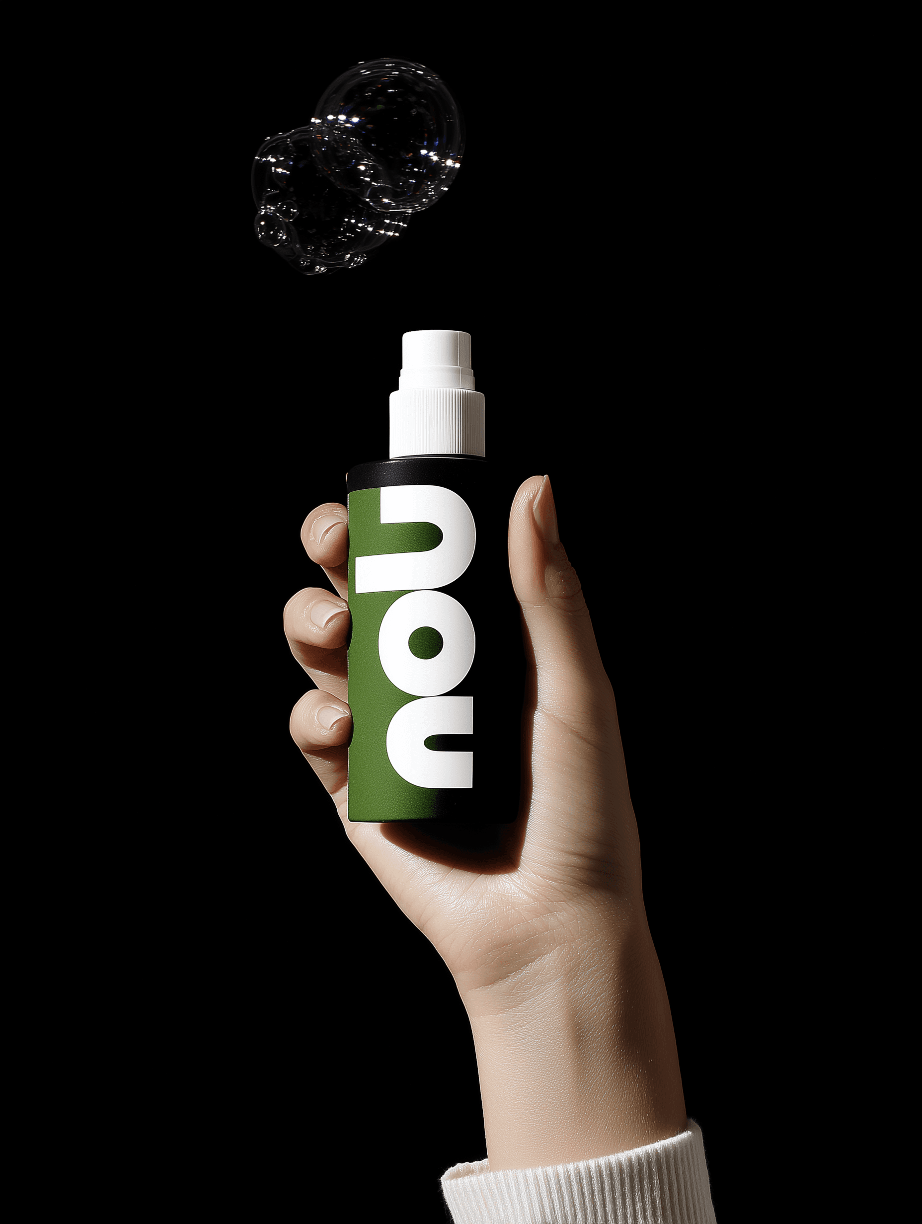 Hand holding a minimalist spray bottle with a green label and bold white typography, releasing a single soap bubble against a black background.