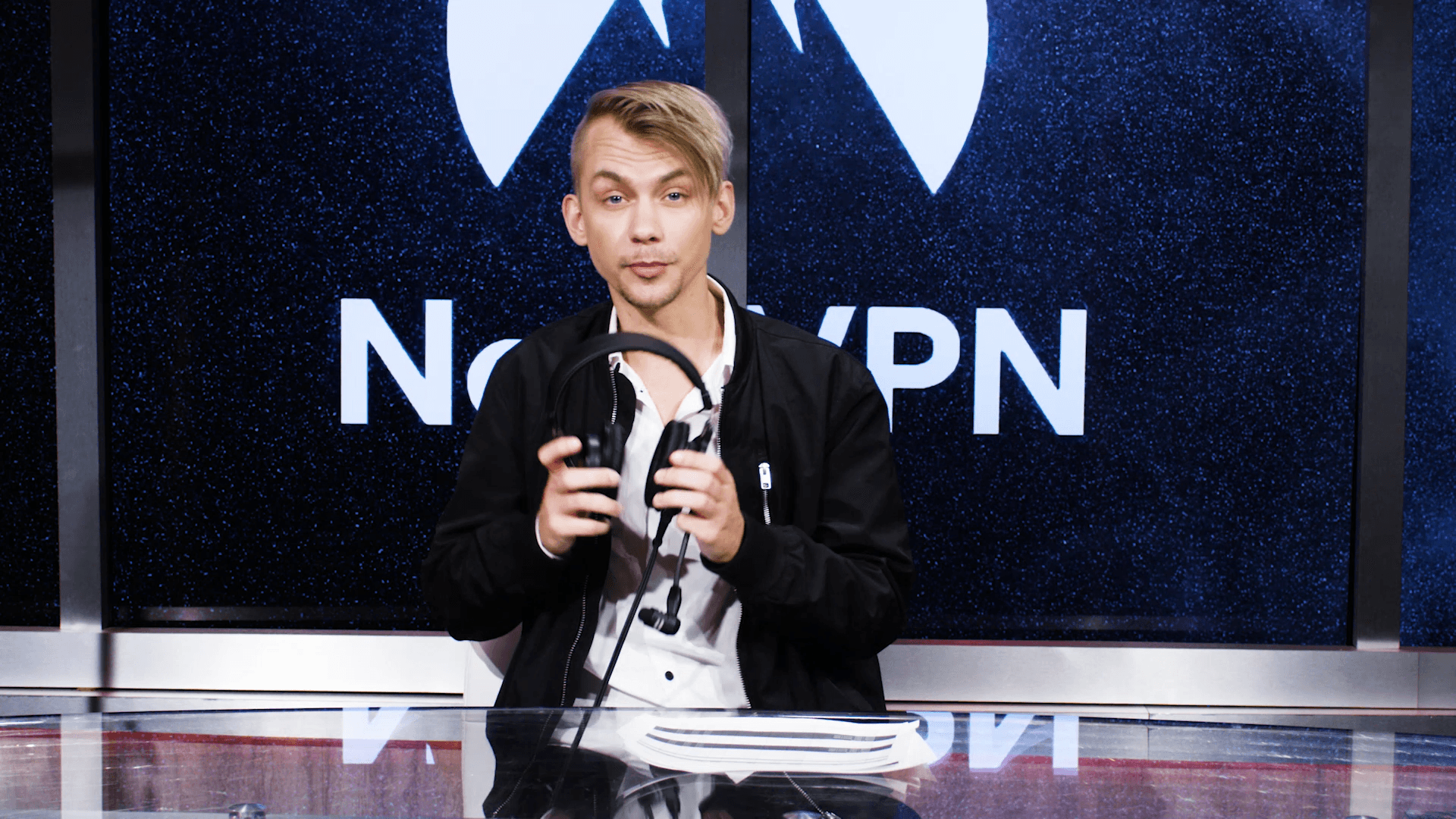 Medium wide shot esports announcer putting on headphones in front of Nord VPN logo in background.