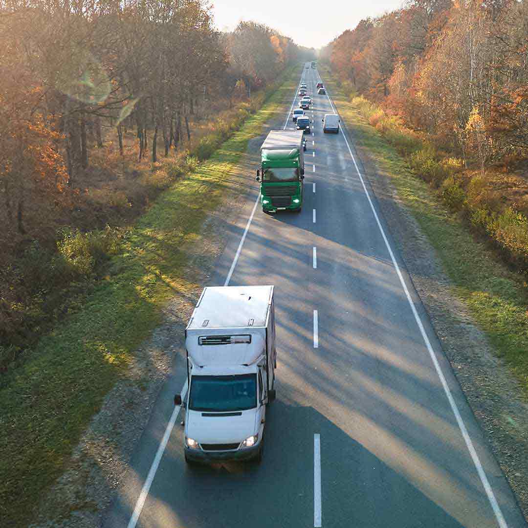 Вантажні автомобілі та легкові машини рухаються трасою серед лісу — символ наземних перевезень