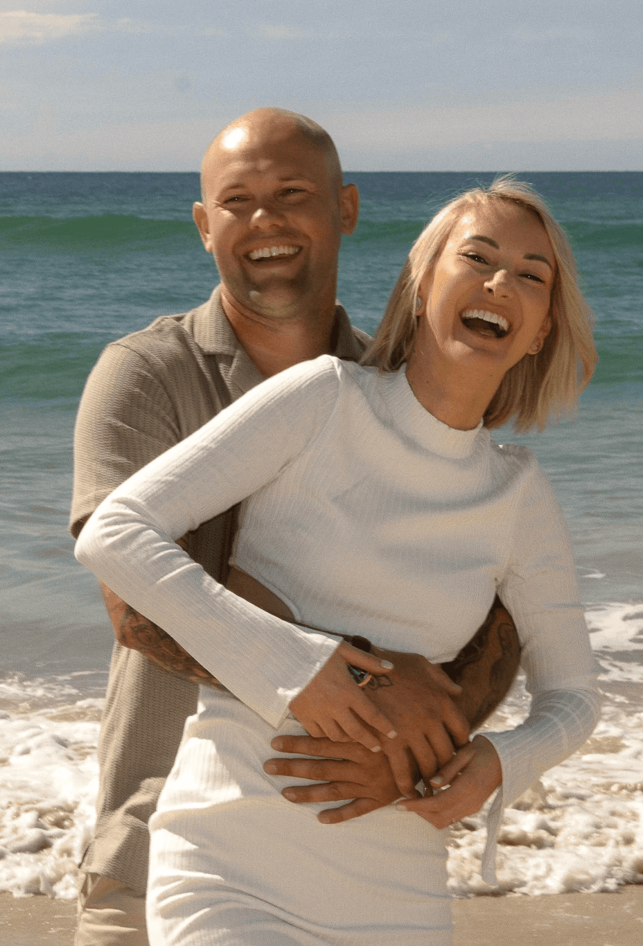 Laughing couple in coordinated neutral outfits during a beach photography session.