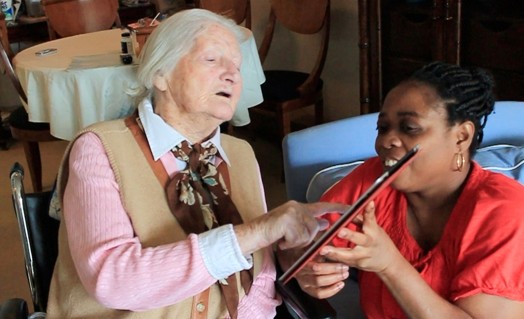 A photo of an old person showing something on a tablet to another one.