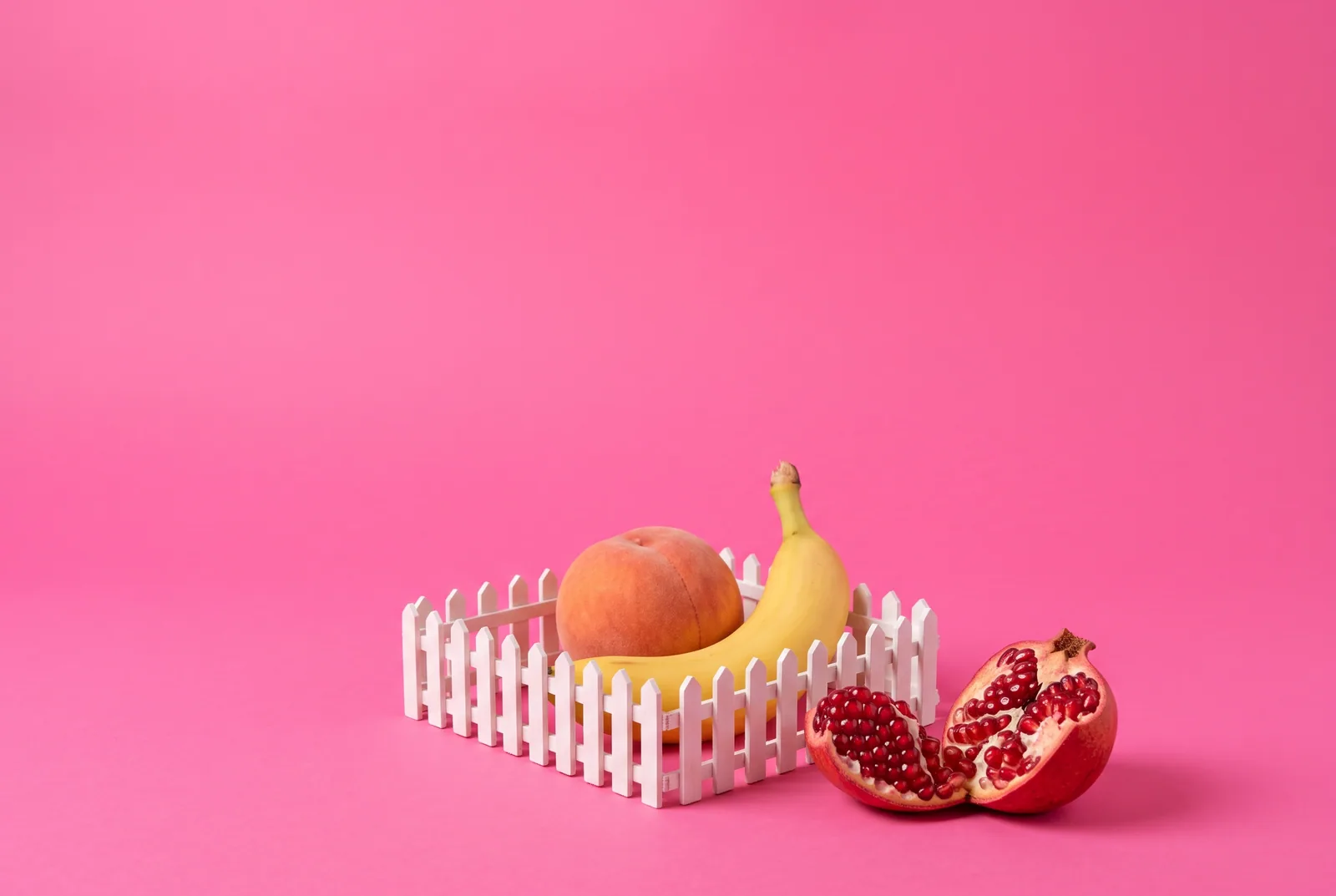 Two pears inside a tiny white picket fence with a flashy pomegranate outside, a metaphor for social media boundaries when a husband looks at women online