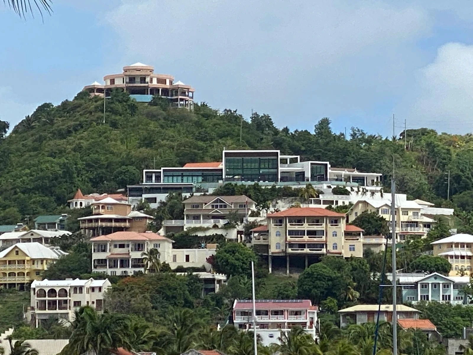 Hillside setting of The Hill Residence in St. Lucia by Atelier International, its modern glass-and-white form standing among traditional Caribbean homes on the slope.