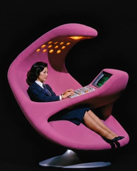A woman sits in a retro pink pod chair with a built-in computer terminal, evoking early Mac-era backup technology