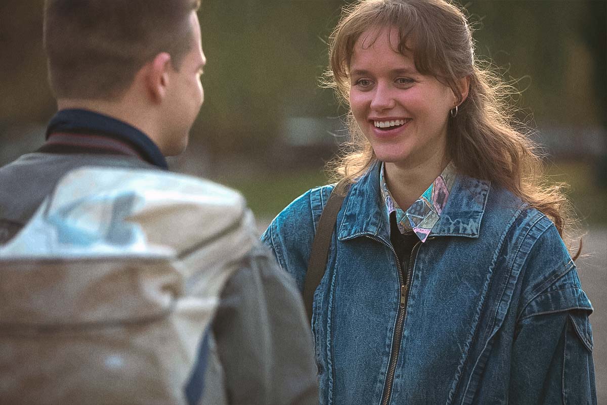 Rimants (Džiugas Grinys) and Monika (Digna Kulionytė) laughing together, capturing young love in the Baltic 90s coming-of-age film Southern Chronicles.