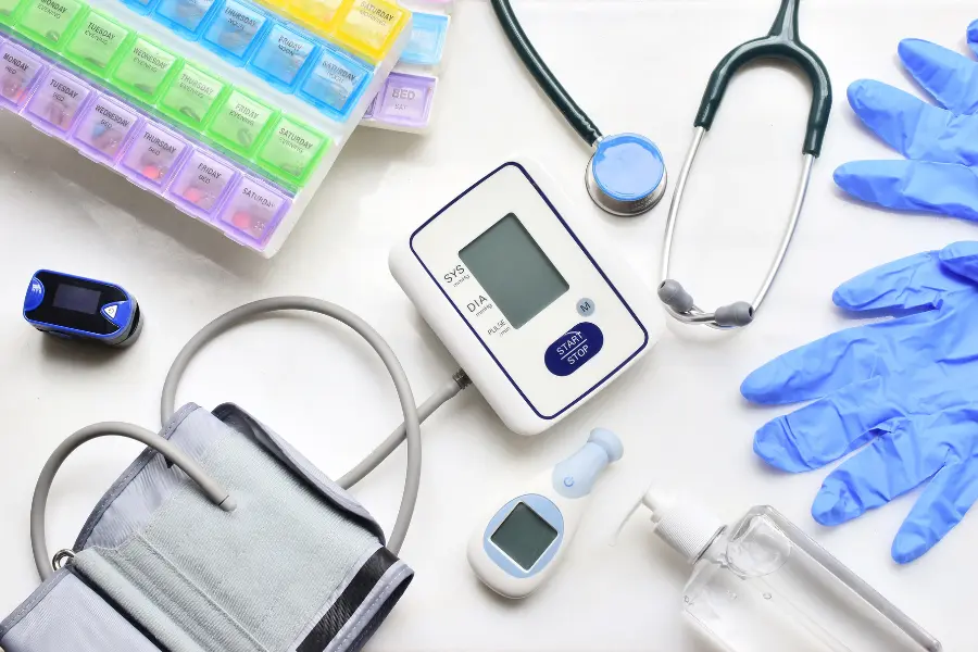 AI medical coding tools laid out alongside a blood pressure monitor, stethoscope, pulse oximeter, weekly pill organizer, and blue latex gloves on a white surface.