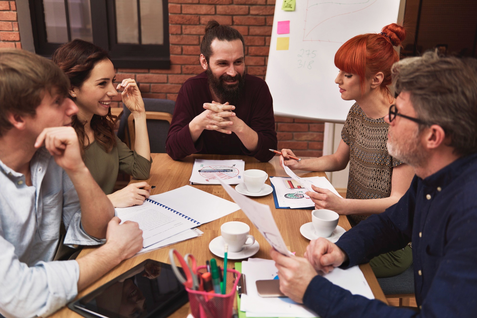 Group of professionals in a workshop setting discussing charts and notes around a table with coffee.