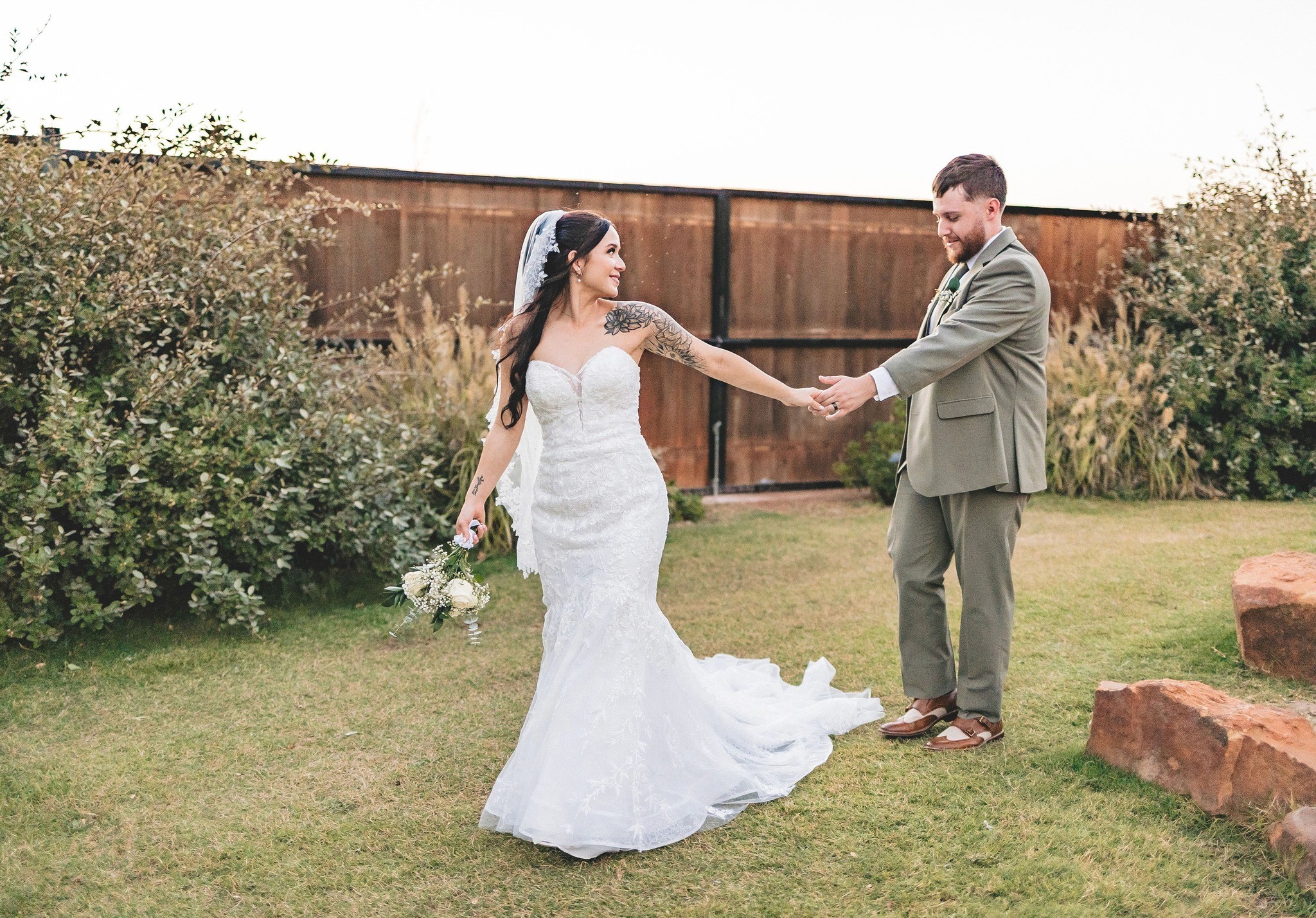 A joyful married couple stands back-to-back outdoors.