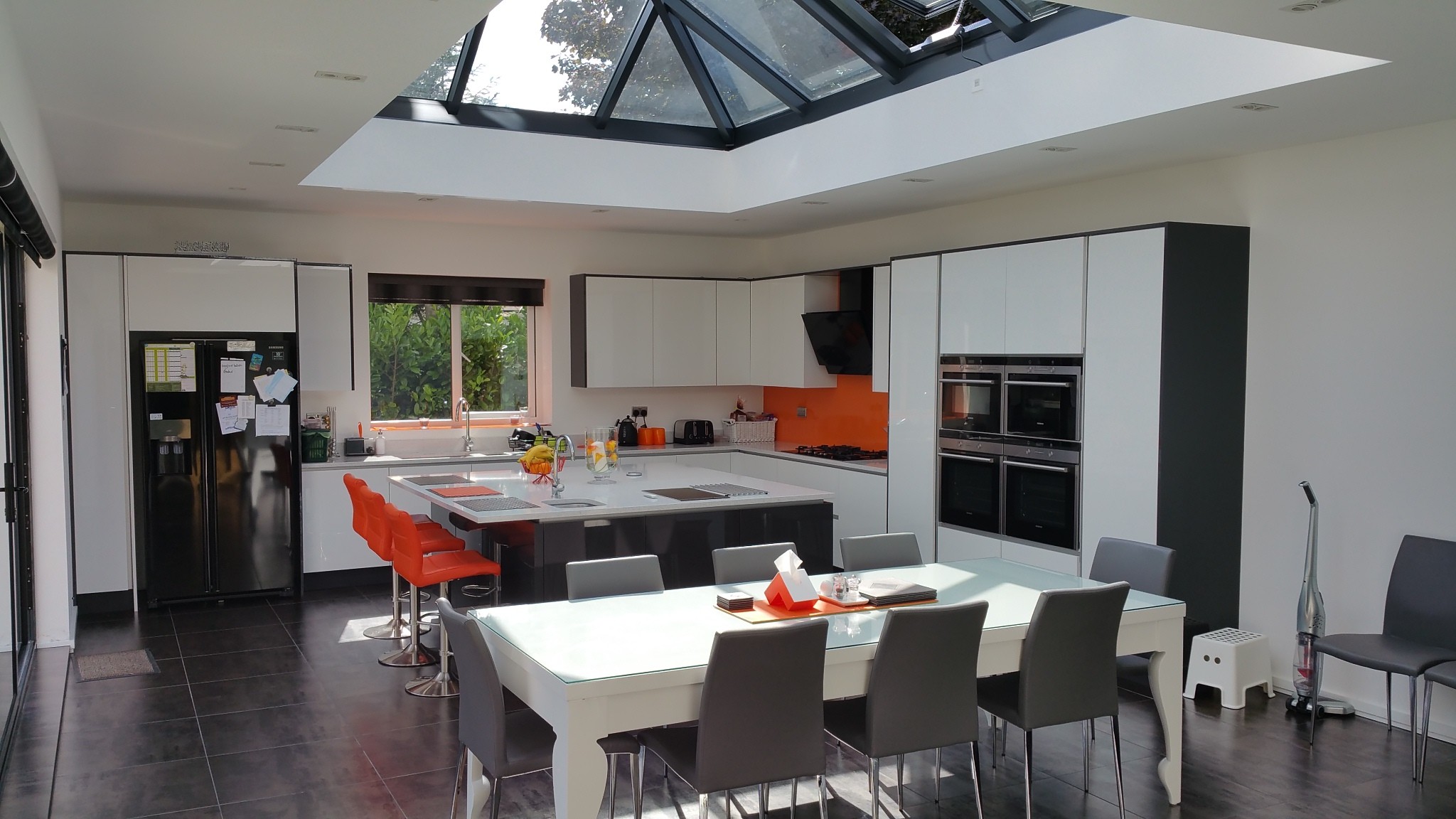 Large open-plan kitchen and dining space within orangery extension, featuring central roof lantern, modern cabinetry, and garden views.
