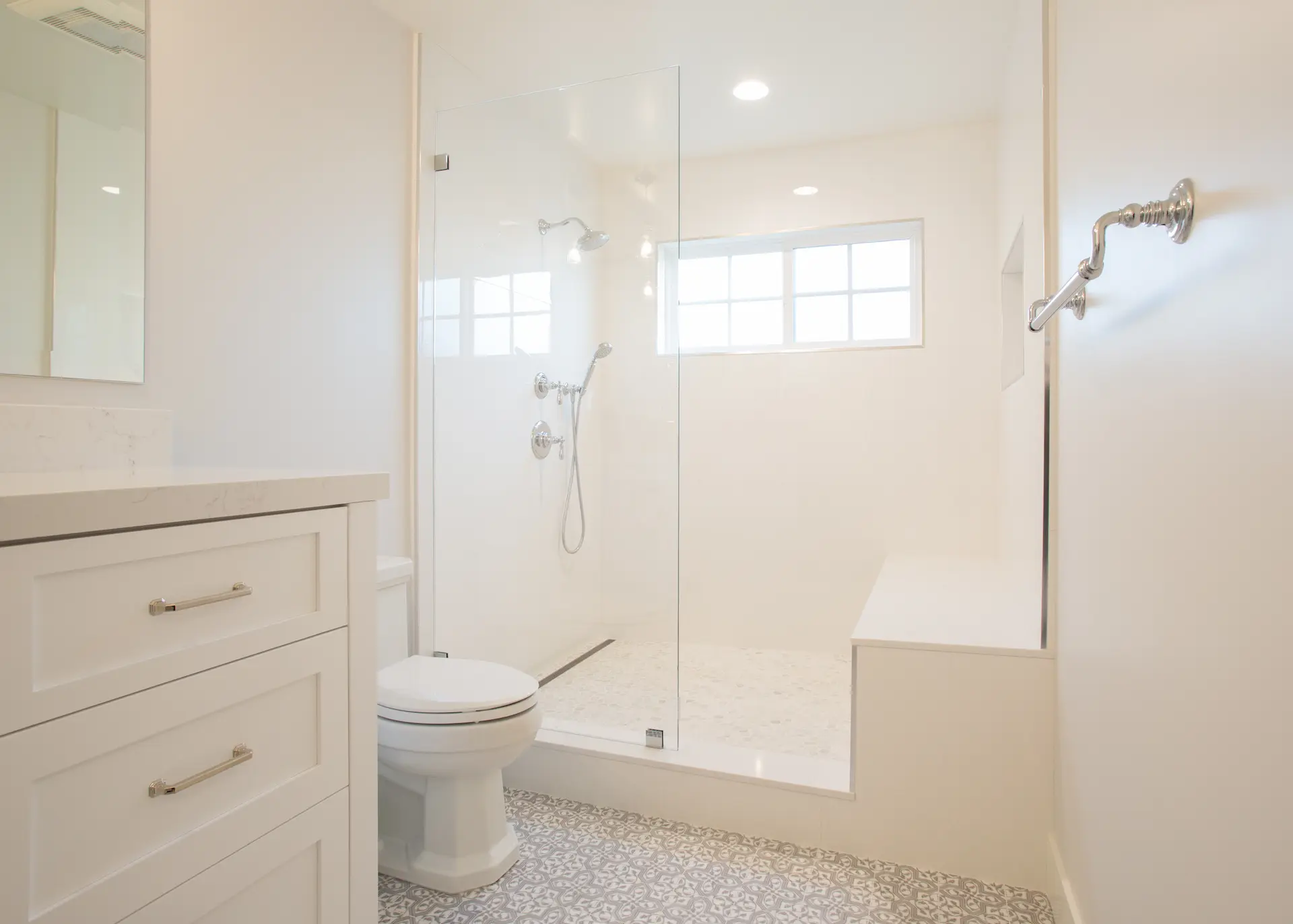 Close-up of luxurious bathroom with soft tones, custom vanity, and spacious walk-in shower with bench. From Dana Point Cape Cod remodel, photo by Chris Darnall.