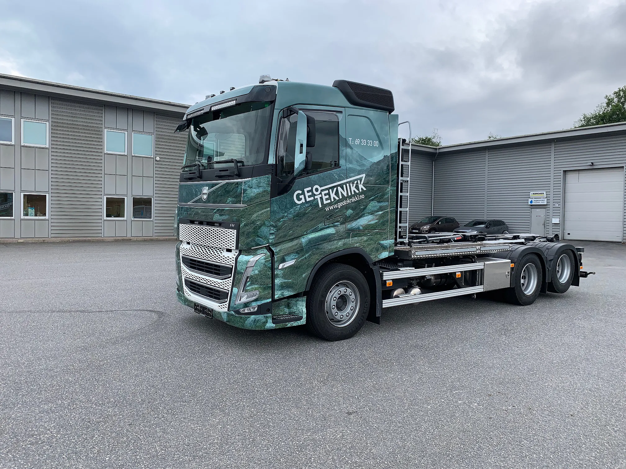 Lastebil med foliering i grønt fjellmotiv og logo for Geoteknikk på førerhuset, parkert utendørs