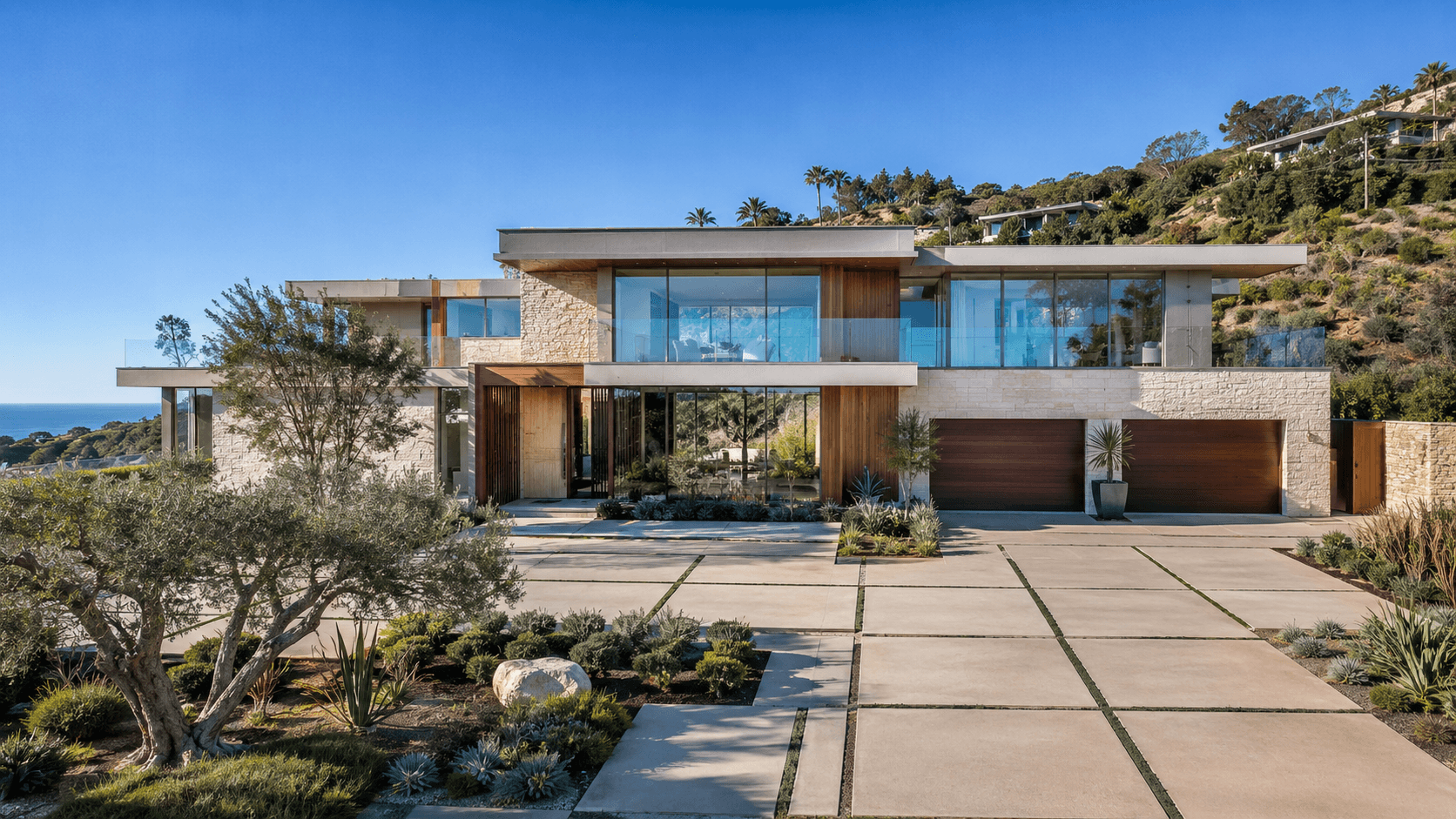 Modern stone and wood villa on a hillside with an ocean view driveway