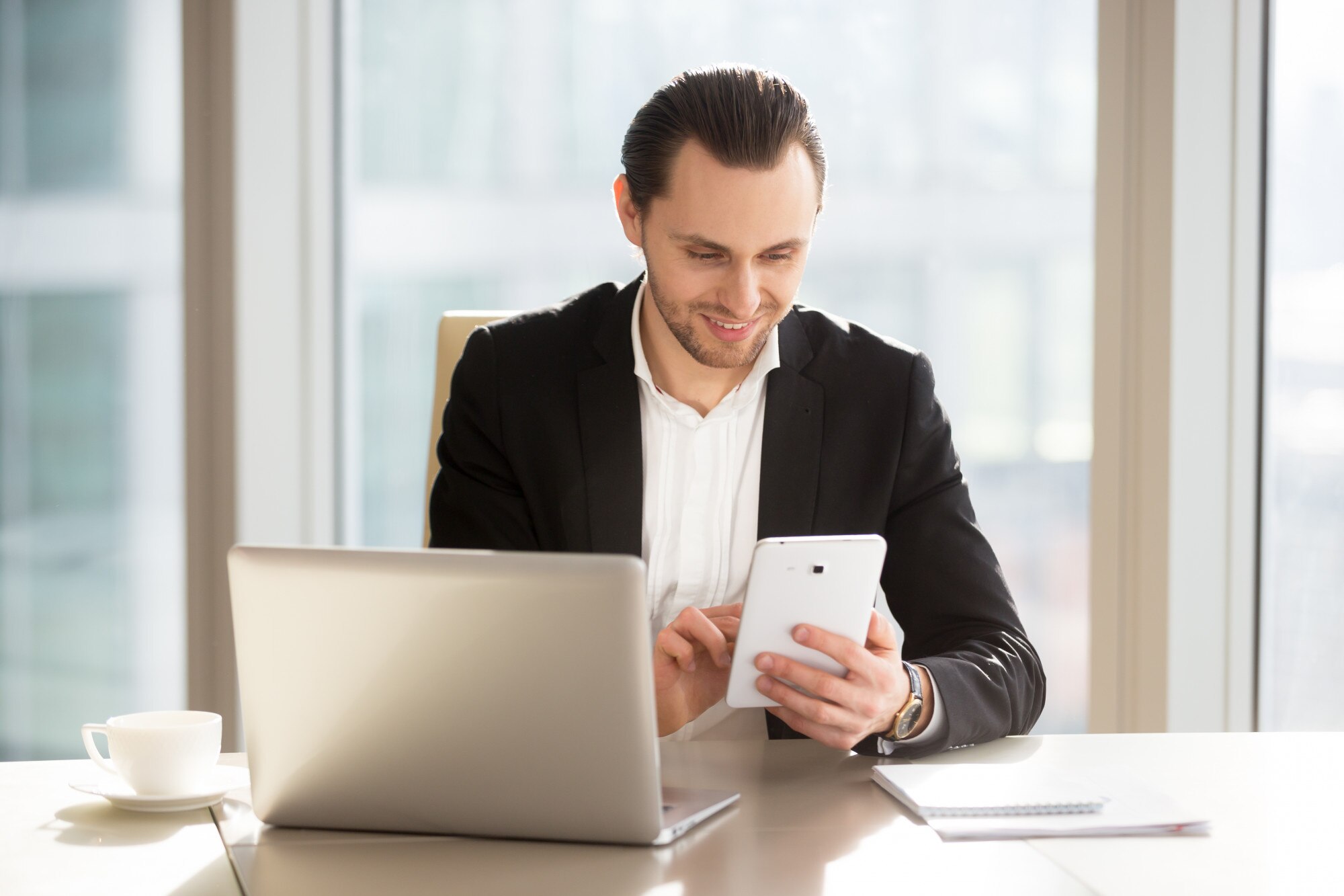 Makelaar aan bureau met laptop en tablet, moderne kantooromgeving