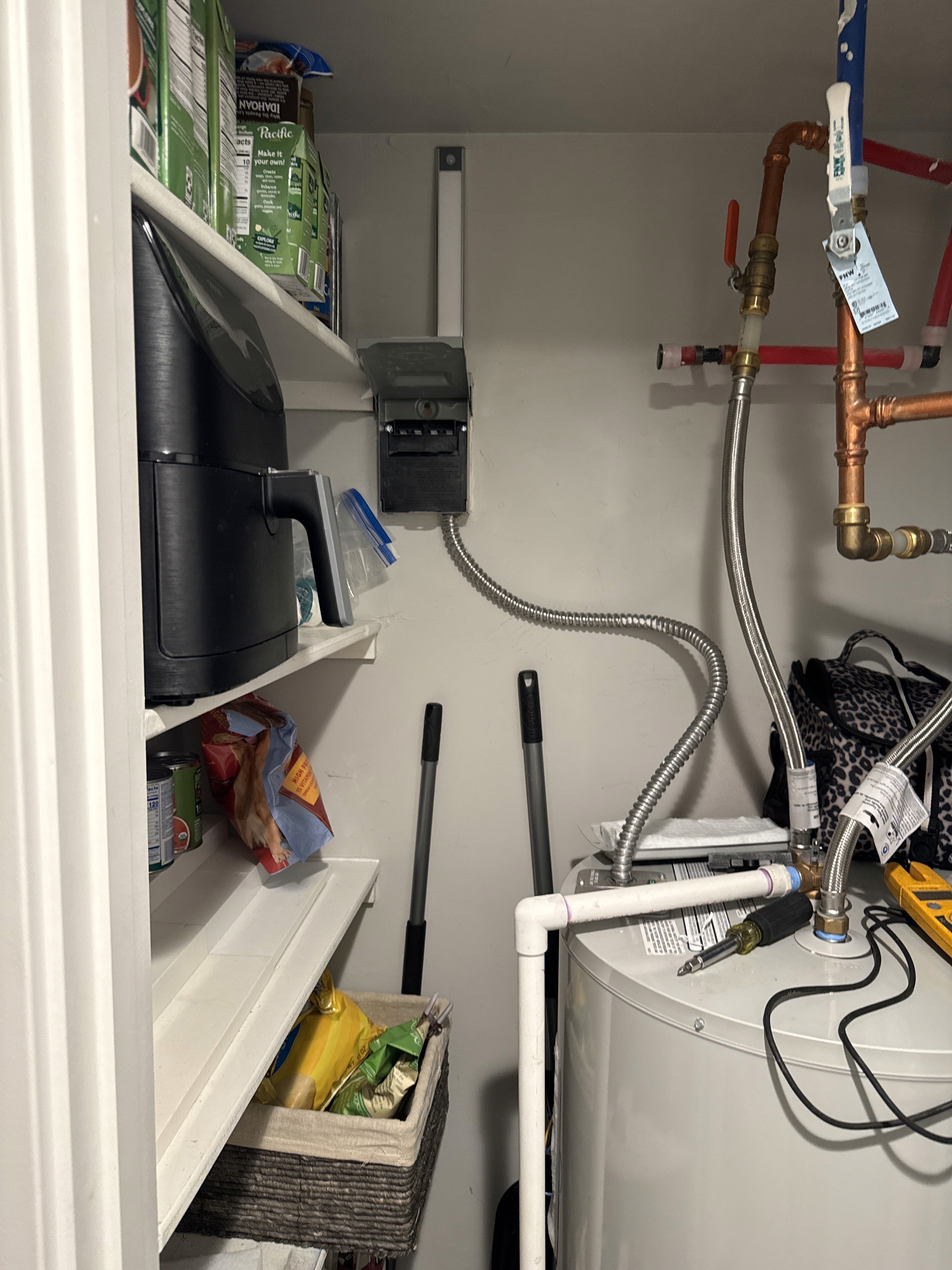The image shows a utility closet containing a water heater and a sump pump system. A sump pump is a device installed in the lowest part of a home to remove accumulated water and prevent basement or crawlspace flooding. 