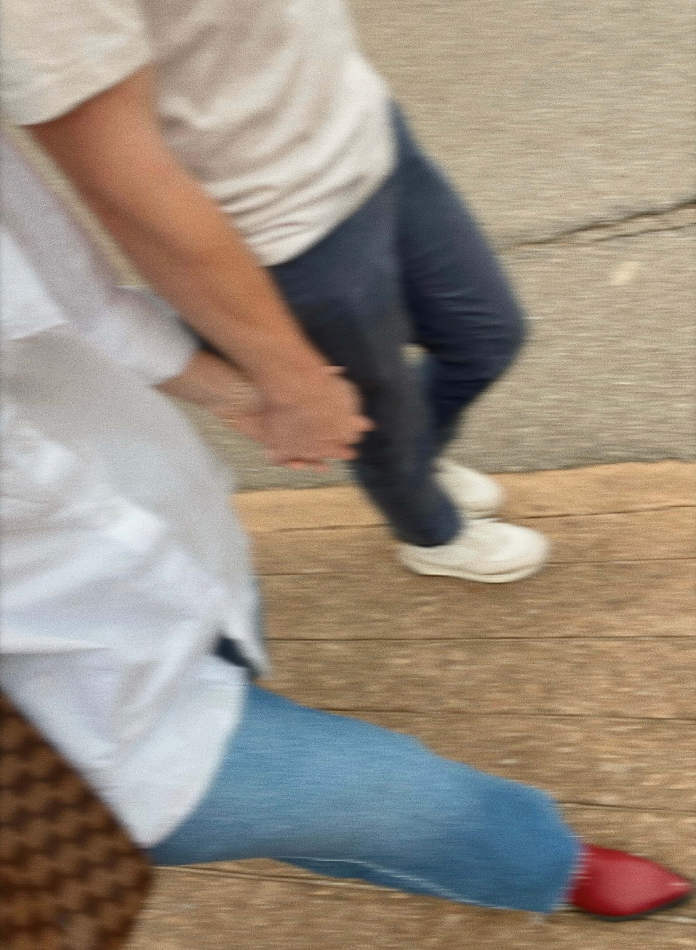 a blurry photo of two people strutting down the street. They're only visible from their torsos down. The woman is wearing red cowboy boots