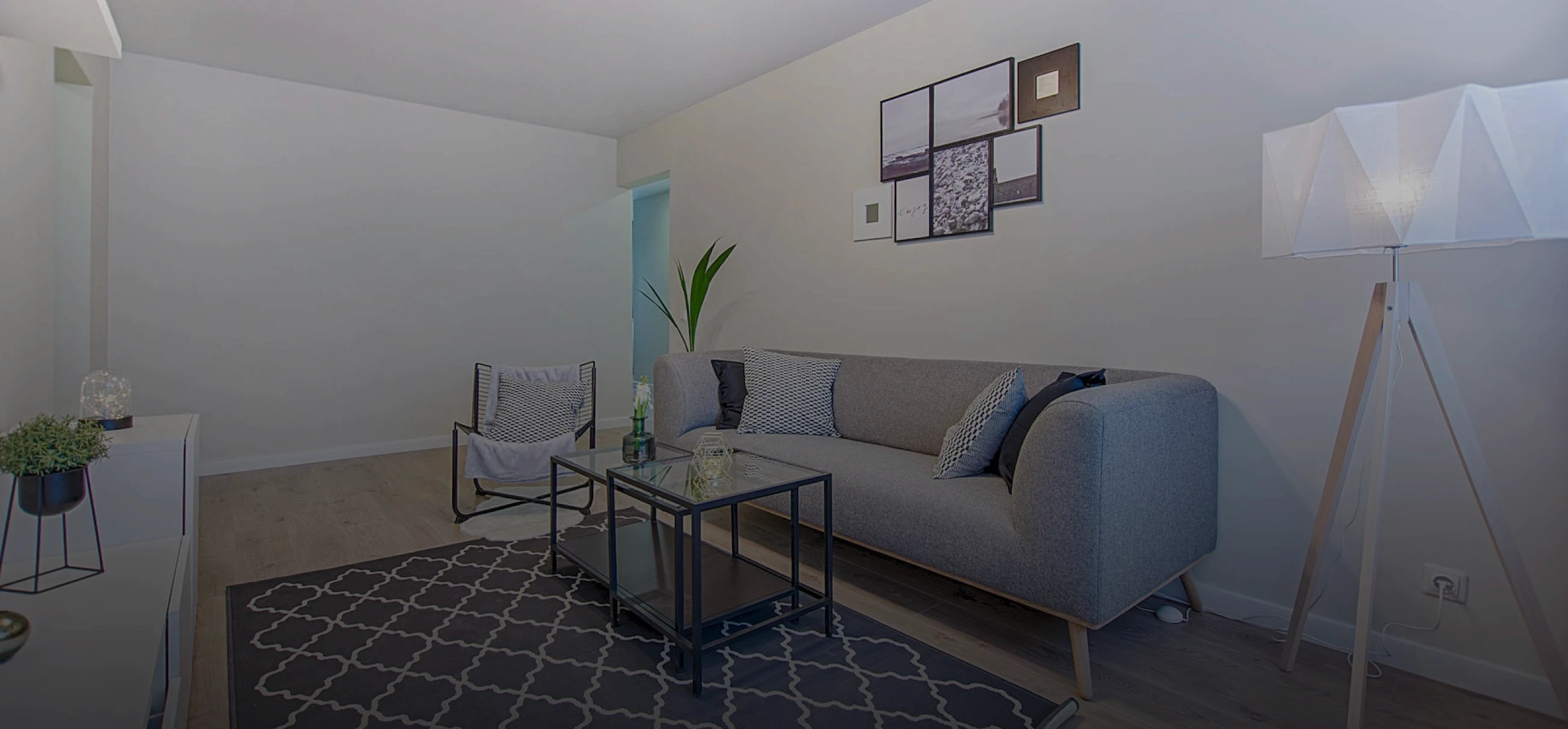 imagem de sala de estar projetada. Na imagem contém cores pastéis e cores nêutras como cinza e branco. Temos na imagem um sofá, quadros na parede, uma mesa de centro acima de um tapete quadriculado.
