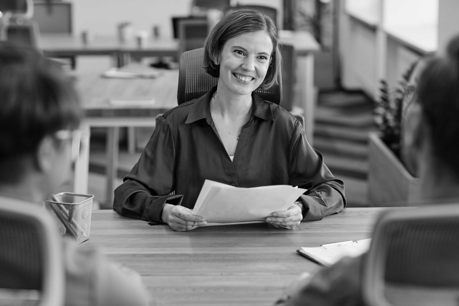 Recruiter smiling during a job interview, holding documents at an office table.