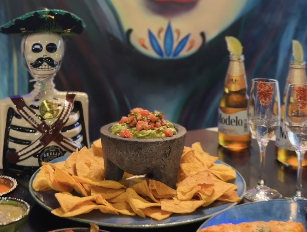 Three thick, grilled burritos or wraps, filled with seasoned meat, visible vegetables, and herbs, served side-by-side on a dark plate with small bowls of salsa and diced tomatoes in the background.