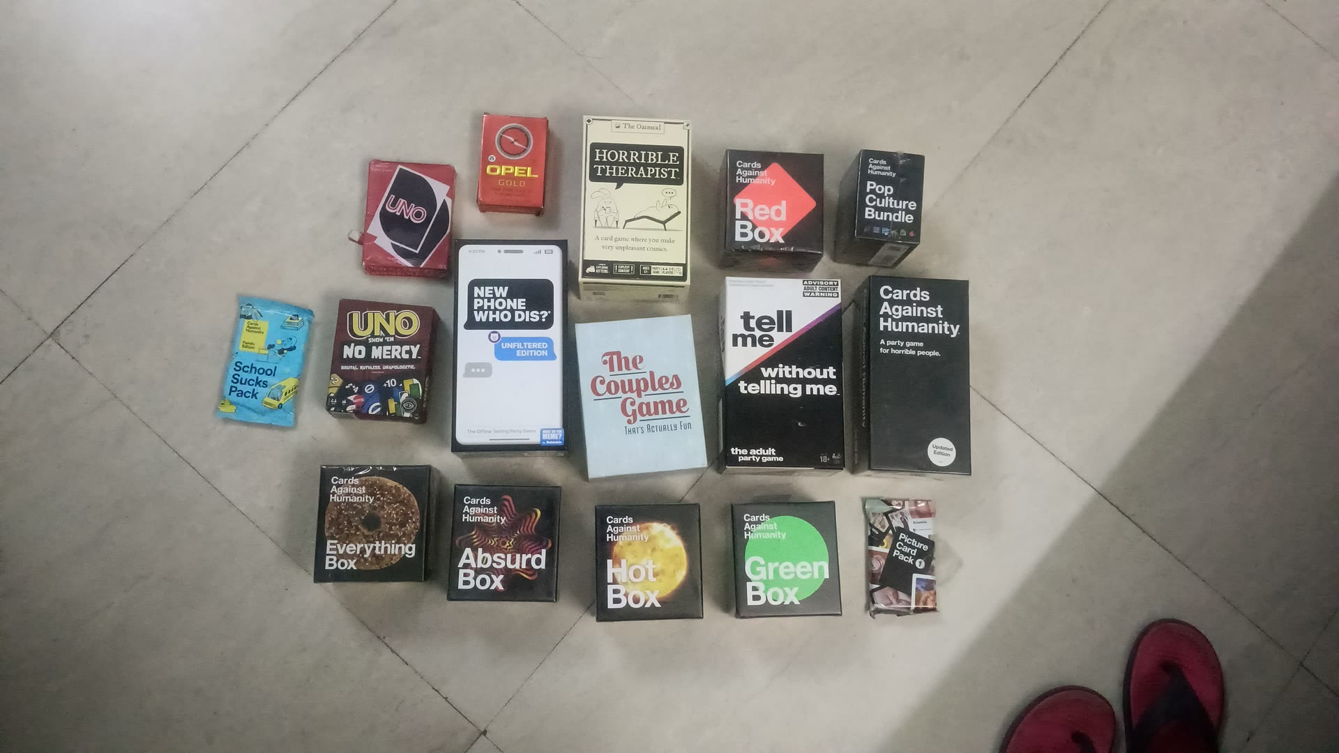 A collection of card and party games, including Cards Against Humanity boxes, UNO, and The Couples Game, arranged together on a tiled floor.
