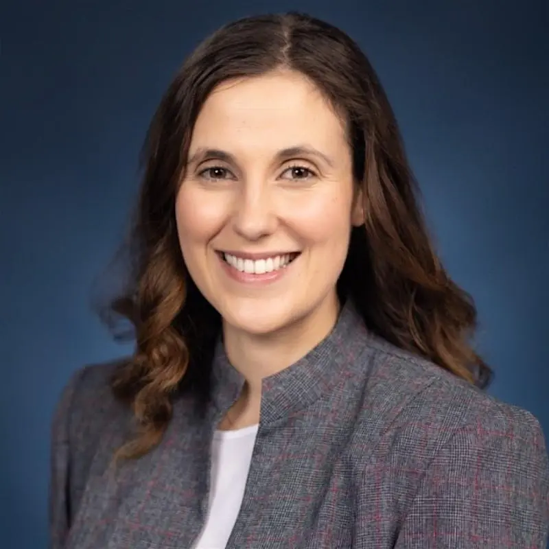 A confident person with short, styled hair and a leather jacket poses against a dark backdrop.