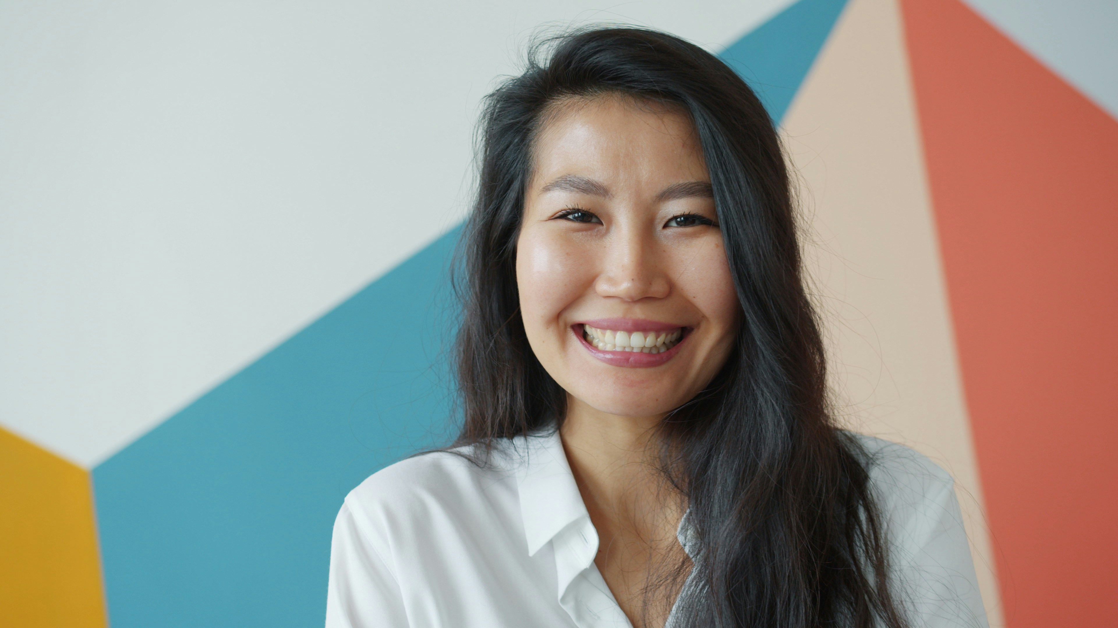 Smiling woman with long dark hair against colorful wall